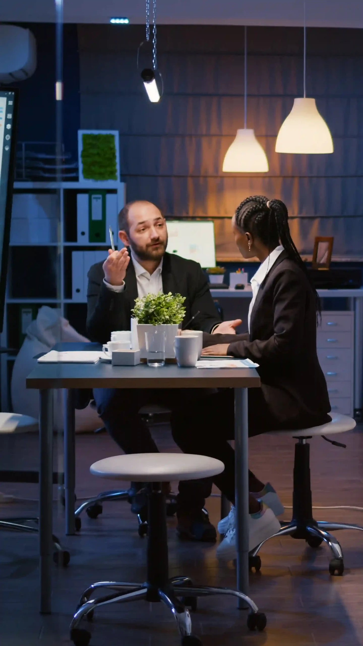 A professional man and woman discussing at a modern office table with dim lighting.
